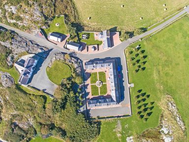 An aerial view of a square building with an inner courtyard surrounded by grass and trees at Tyn Towyn - The Stables in Trearddur Bay