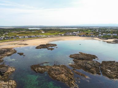 A coastal landscape with rocky shoreline sandy beach and houses near the shore at Tyn Towyn - The Stables in Trearddur Bay
