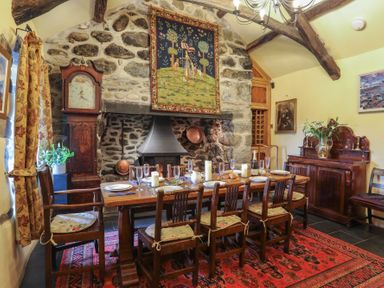 A dining room with a wooden table set for six and a stone fireplace at Tyddyn Morthwyl in Criccieth