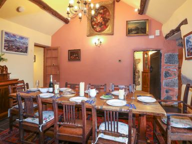 A dining room with a wooden table set with plates glasses and candles and wooden chairs at Tyddyn Morthwyl in Criccieth