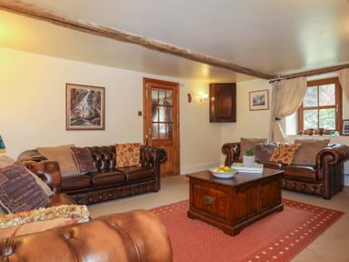A living room with brown leather sofas wooden coffee table and window at Tyddyn Morthwyl in Criccieth