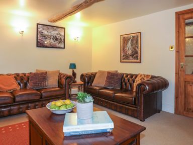 A living room with two leather sofas a wooden coffee table with books and a plant and framed paintings on the walls at Tyddyn Morthwyl in Criccieth