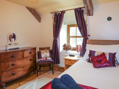 A bedroom with a wooden dresser a window with purple curtains and a bed with pillows at Tyddyn Morthwyl in Criccieth