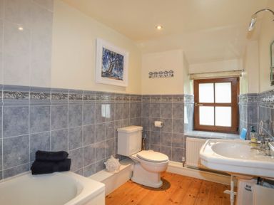 A bathroom with a toilet sink bathtub wooden floor and a window at Tyddyn Morthwyl in Criccieth