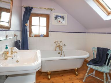 A bathroom with a clawfoot bathtub a sink a wooden chair with a towel and a window at Tyddyn Morthwyl in Criccieth
