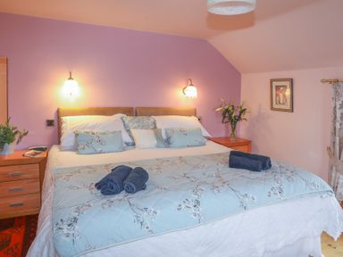 A bedroom with a double bed bedside tables lamps and flowers at Tyddyn Morthwyl in Criccieth