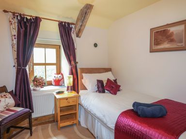 A bedroom with a single bed side table chair and window with curtains at Tyddyn Morthwyl in Criccieth