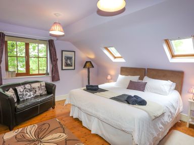 A bedroom with a large bed two skylight windows a black leather sofa and a carpet at Tyddyn Morthwyl in Criccieth