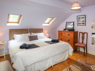 A bedroom with a large bed under two skylights and a wooden dresser with a mirror at Tyddyn Morthwyl in Criccieth