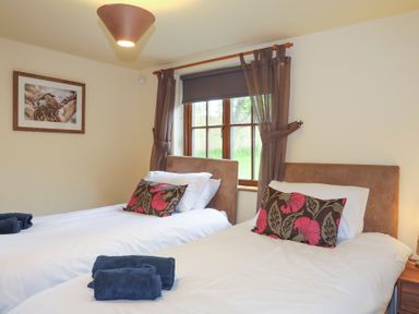 A bedroom with two single beds each with a decorative pillow and folded towels on top at Tyddyn Morthwyl in Criccieth