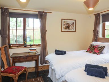 A bedroom with two single beds a wooden desk and chair next to windows with curtains at Tyddyn Morthwyl in Criccieth