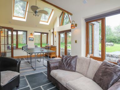 A room with a sofa chair table tennis table and large windows at Tyddyn Morthwyl in Criccieth