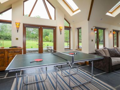 A recreational room with a ping pong table and couch near windows and glass doors at Tyddyn Morthwyl in Criccieth