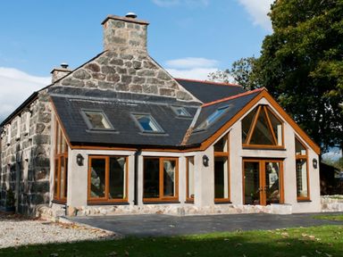 Stone house with large windows and a patio in front at Tyddyn Morthwyl in Criccieth
