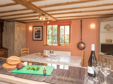A kitchen with a cutting board holding bread onion garlic and peppers and a table set with breakfast items at Tyddyn Morthwyl in Criccieth