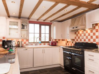 A kitchen with wooden cabinets a black stove a red toaster and a window above the sink at Tyddyn Morthwyl in Criccieth