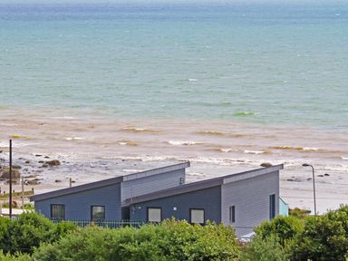 A coastal scene with modern houses near the shore and ocean waves behind at Ty Glyn in Criccieth