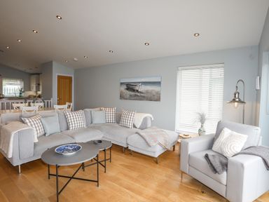 A living room with a gray sectional sofa and armchair a coffee table and a painting on the wall at Ty Glyn in Criccieth