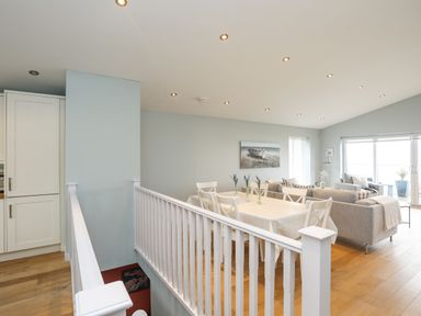 A dining table with chairs and vases next to a living area with sofas and sliding glass doors at Ty Glyn in Criccieth