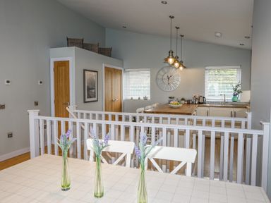 A kitchen with wooden doors white chairs and three vases with flowers on the table at Ty Glyn in Criccieth
