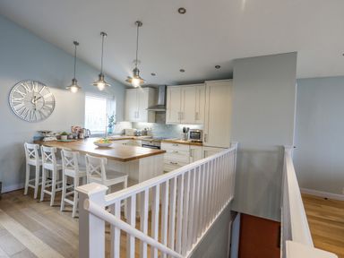 A kitchen with wooden countertops white cabinets four white chairs and hanging lights at Ty Glyn in Criccieth