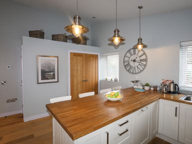 A kitchen with wooden countertops white cabinets fruit bowl and hanging lights at Ty Glyn in Criccieth