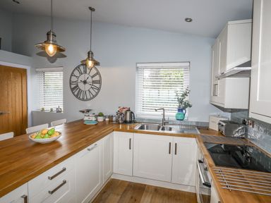 A kitchen with white cabinets wooden countertops a sink stove and a large wall clock at Ty Glyn in Criccieth