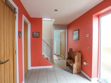A hallway with coral walls a wooden bench a door to a stairway and an open door showing a room at Ty Glyn in Criccieth