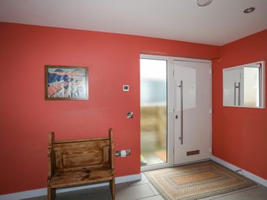 An entryway with a wooden bench under a framed picture a white front door with frosted glass panels and a rectangular rug on the floor at Ty Glyn in Criccieth