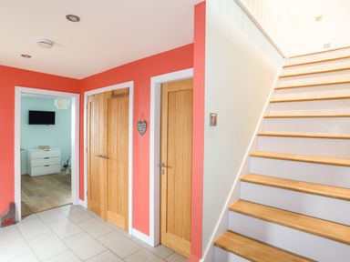 A hallway with tiled floor wooden doors and stairs next to a bedroom with a dresser and wall-mounted TV at Ty Glyn in Criccieth