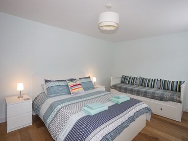 A bedroom with a double bed and bedside tables with lamps next to a daybed with striped cushions at Ty Glyn in Criccieth