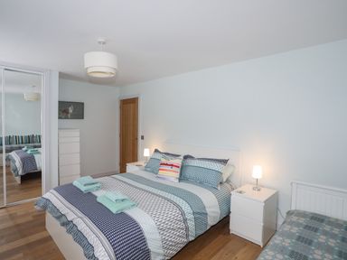 A bedroom with a double bed with patterned bedding and folded towels on top next to two white bedside tables with lamps at Ty Glyn in Criccieth