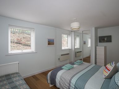 A bedroom with a bed, chest of drawers, mirrored wardrobe, two windows with blinds and framed pictures at Ty Glyn in Criccieth