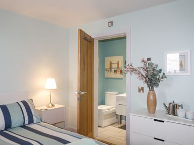 A bedroom with a striped bedspread a bedside table with a lamp and an open door leading to a bathroom at Ty Glyn in Criccieth