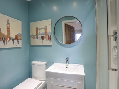 A bathroom with a toilet and a sink under a round mirror with paintings of london landmarks on the wall at Ty Glyn in Criccieth