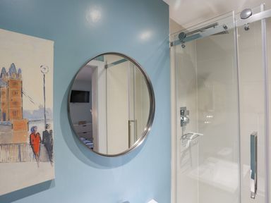 A bathroom with a round mirror on a blue wall and a glass shower enclosure at Ty Glyn in Criccieth