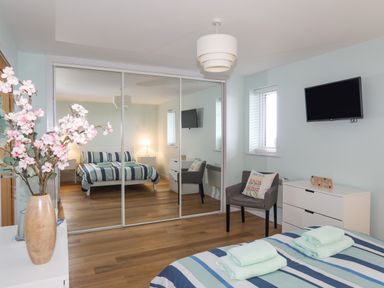 A bedroom with a bed striped bedspread towels on bed mirrored wardrobe and a TV on the wall at Ty Glyn in Criccieth