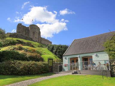 An old stone castle on a grassy hill with a building and outdoor seating area at Ty Glyn in Criccieth