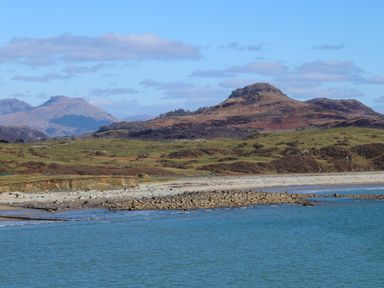A coastal landscape with a rocky beach and grassy hills with mountains in the background at Ty Glyn in Criccieth