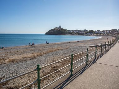 A pebble beach with people near the shoreline and a castle on a hill in the background at Ty Glyn in Criccieth