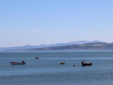 Several boats floating on calm water with hills in the background at Ty Glyn in Criccieth