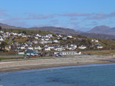 A coastal town with houses on a hillside near a beach and mountains in the background at Ty Glyn in Criccieth