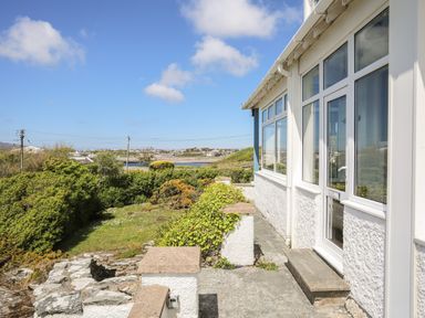 Exterior view of a building with white walls and windows overlooking a garden and distant buildings at Ty Llwyd in Trearddur Bay