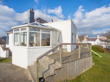 A white house with a sunroom and wooden deck with railings in a garden at Ty Llwyd in Trearddur Bay