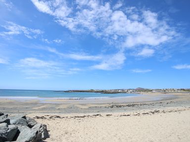 A sandy beach with water rocks and houses in the distance at Trearddur Bay