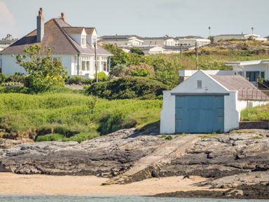 A house with chimneys and a small building with blue doors near a rocky shore at Ty Llwyd in Trearddur Bay