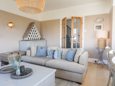 A living room with a beige sofa and blue cushions next to a wooden cabinet with a decorative roof model at Ty Llwyd in Trearddur Bay