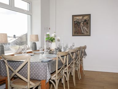 A dining room with a long table covered with a polka dot tablecloth set with plates glasses candles and flowers at Ty Llwyd in Trearddur Bay