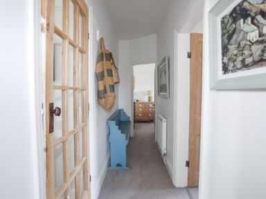 A hallway with a blue bench and bags hanging on hooks leading to a room with a wooden dresser at Ty Llwyd in Trearddur Bay