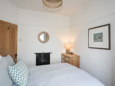 A bedroom with a bed a wooden dresser with a lamp a framed picture and a round mirror at Ty Llwyd in Trearddur Bay